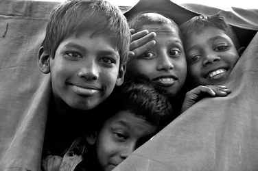 Bambini indigenti guardano attraverso una tela strappata di un furgone della polizia a Dhaka